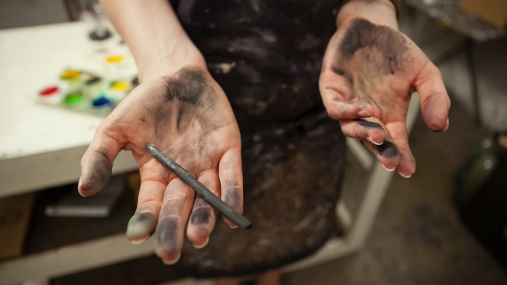 Experimenta con el carboncillo Manos manchadas de carboncillo sosteniendo una barra de dibujo