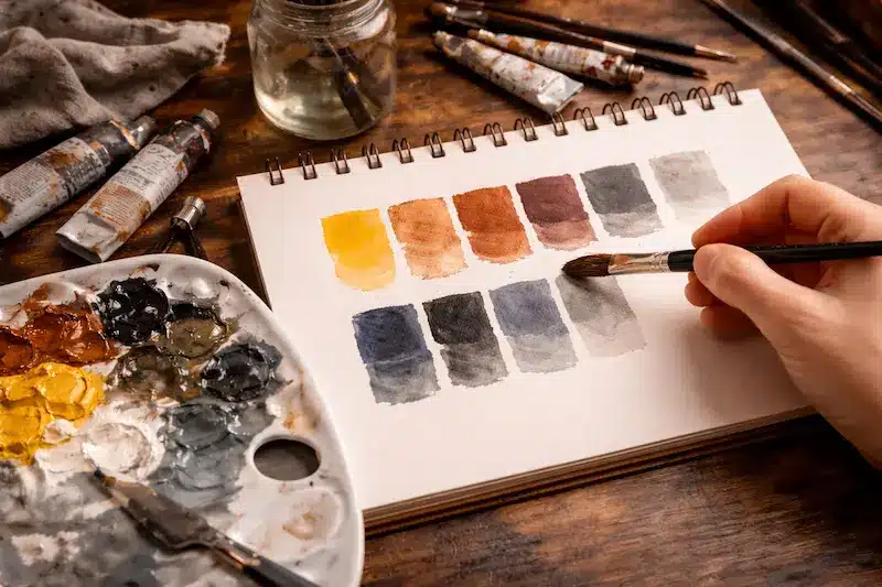 Rutina de práctica semanal para avanzar en pintura sin agobio (30–60 min) — adaptada a óleo, acrílico y acuarela Práctica de escalas de color en un cuaderno con paleta y pinceles
