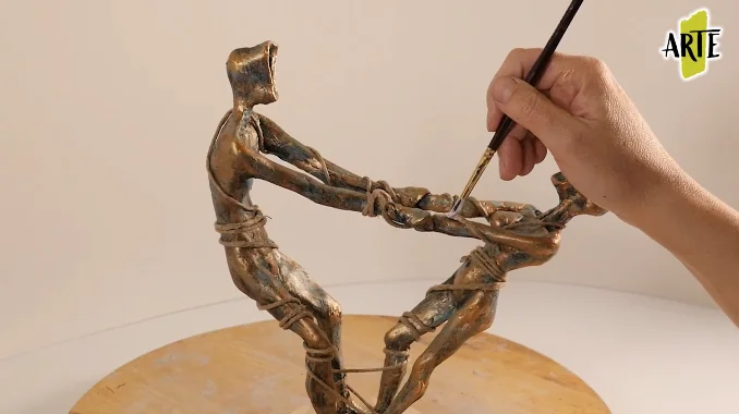 Aplicación con pincel de una pátina sobre dos figuras modeladas con acabado de aspecto bronce