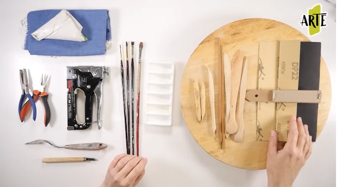 Herramientas de modelado, pinceles, alicates, lija y base de madera preparados sobre la mesa